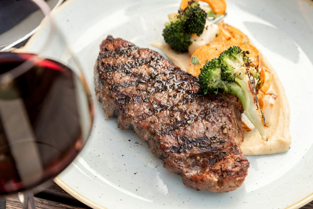 A grilled steak dinner served with a glass of red wine