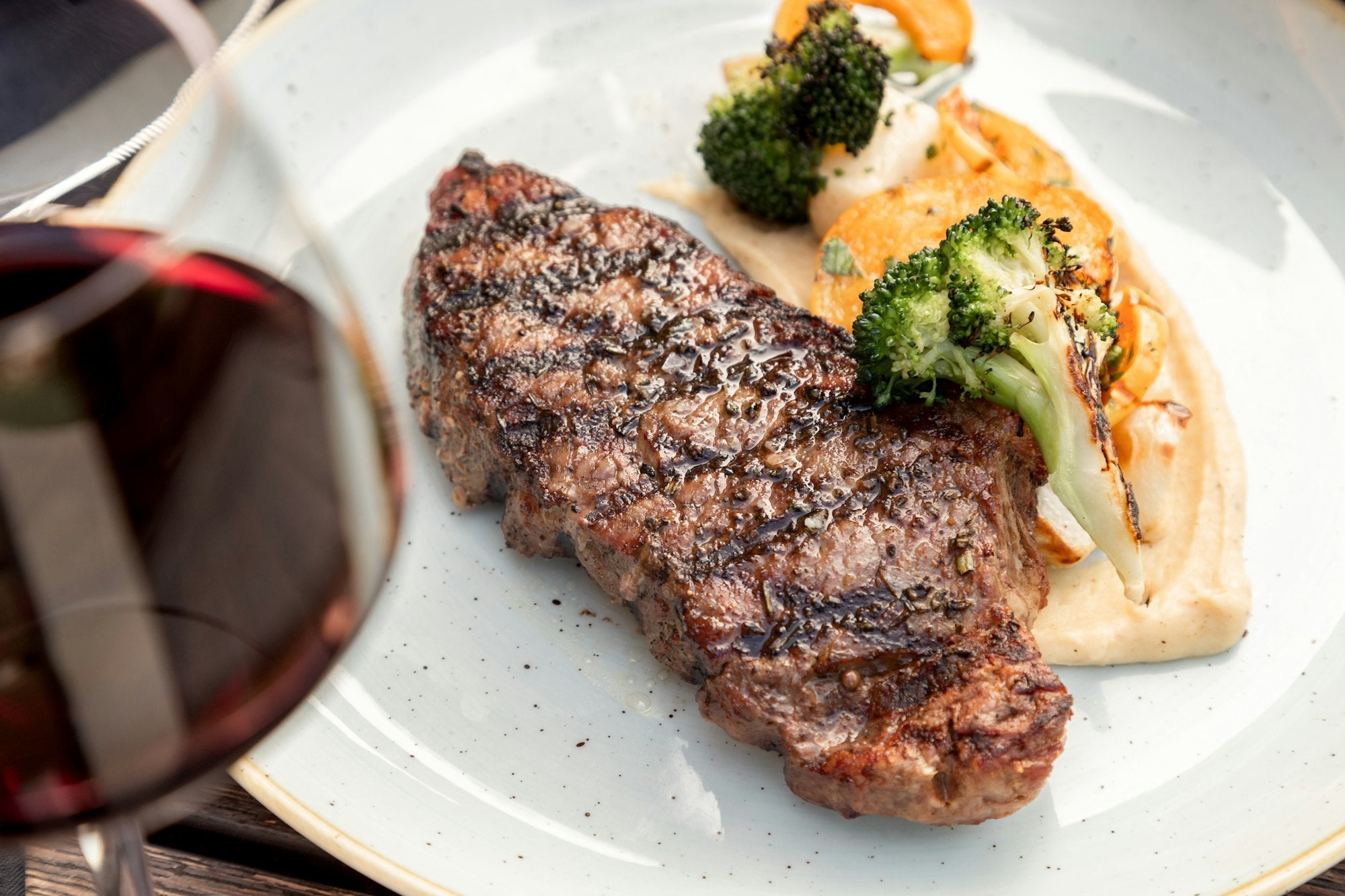 A grilled steak dinner served with a glass of red wine